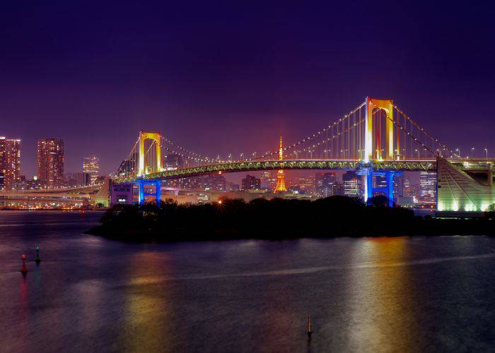 The bright lights of Rainbow Bridge at night, set against the Tokyo skyline.